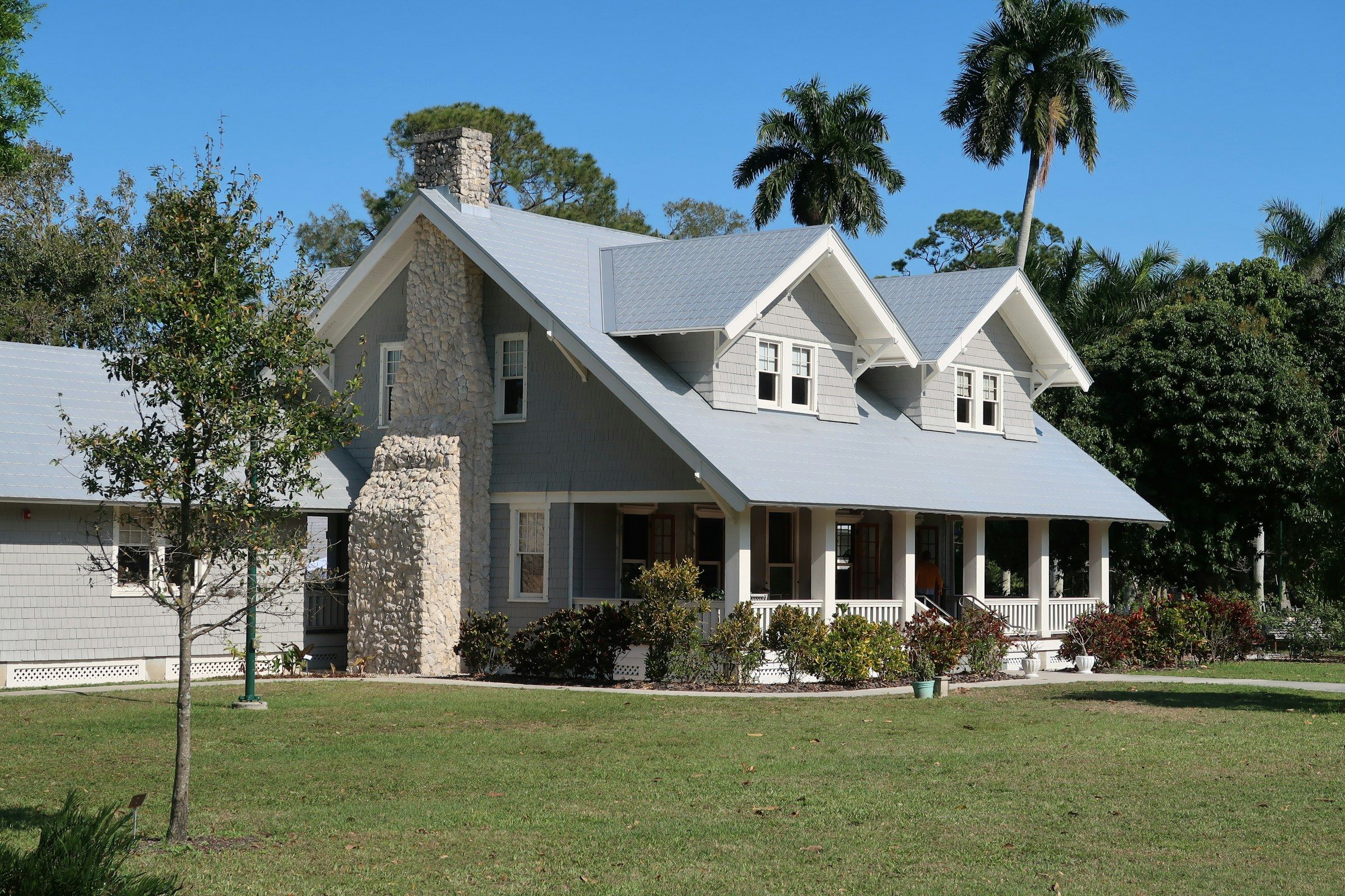 Country home with a wide front porch on a large lawn with palm trees